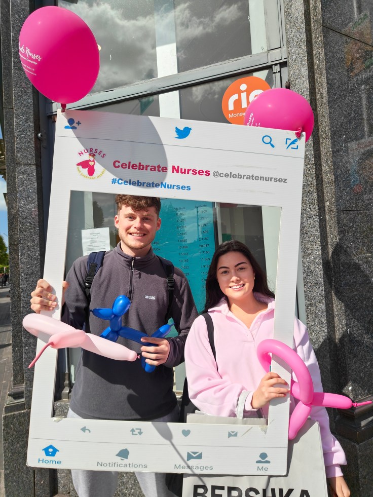 Two members of the public pose with the #CelebrateNurses branded photo frame and balloon animals in Dublin city centre, showing their support for nurse appreciation and International Nurses Day.